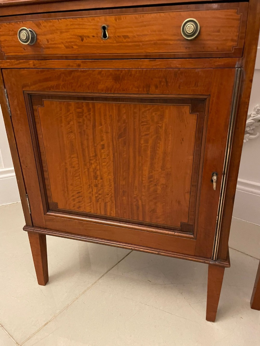 A pair of tall satinwood waterfall bookcases featuring tiered open shelves with brass gallery rails, single drawers, and lower panelled cupboards. View VII