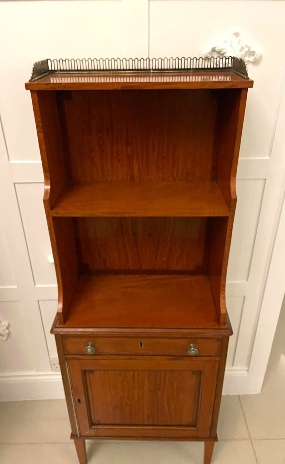 A pair of tall satinwood waterfall bookcases featuring tiered open shelves with brass gallery rails, single drawers, and lower panelled cupboards. View XII