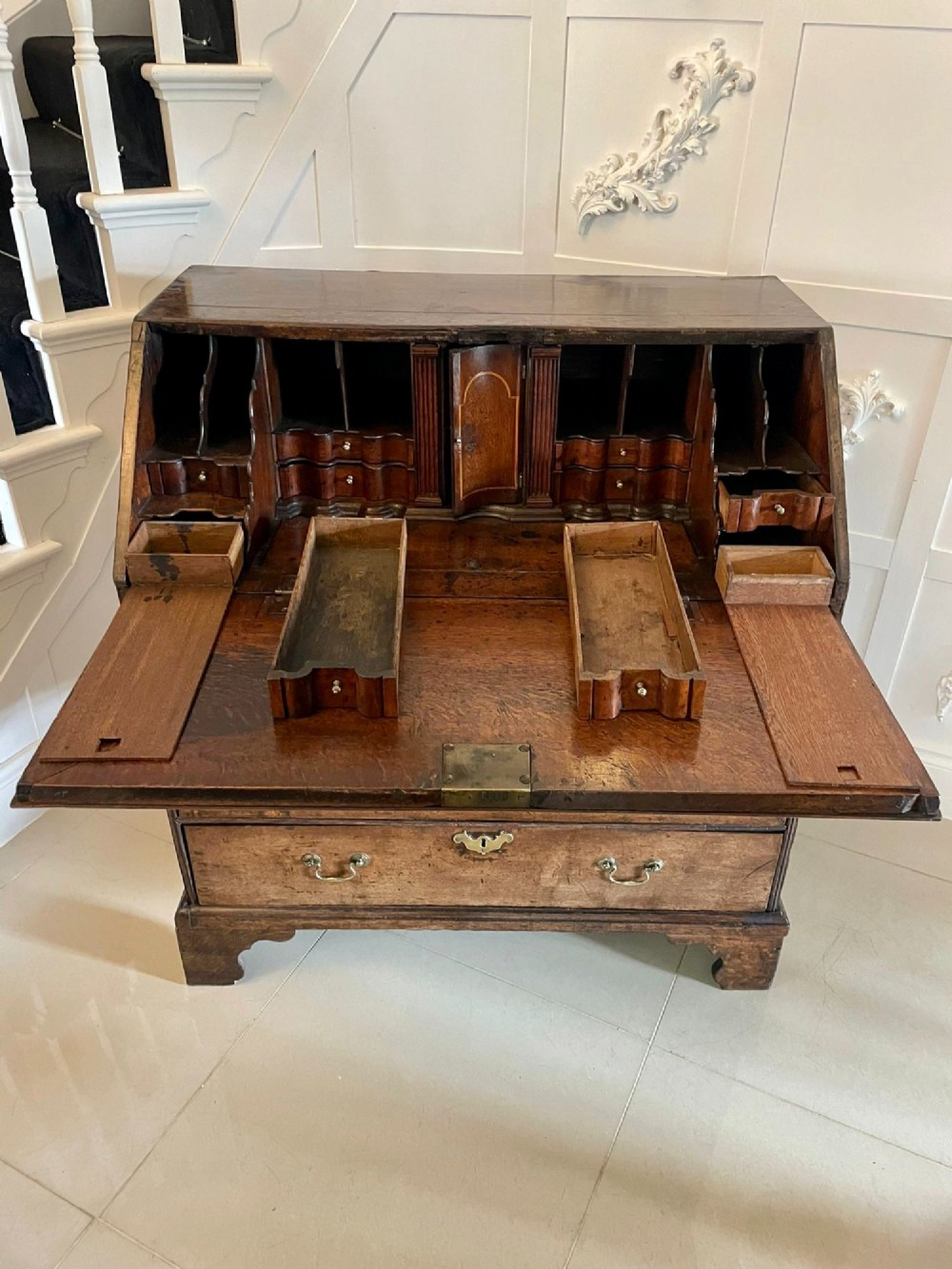 A 17th-century oak writing bureau featuring a slant-front lid above multiple drawers with brass teardrop handles and bracket feet. View IV