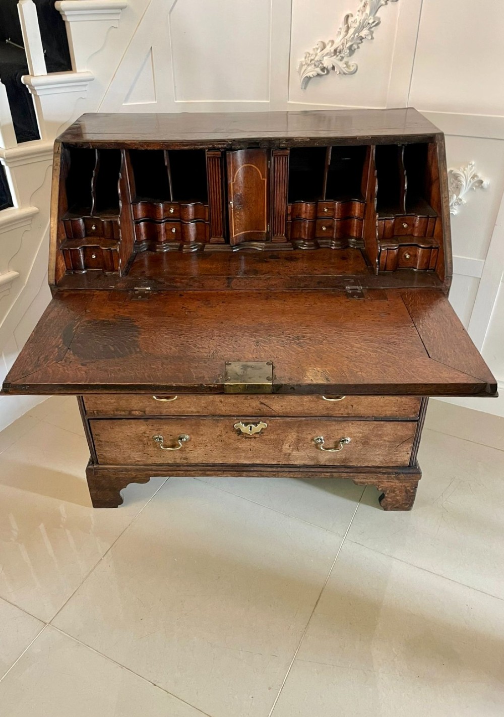 A 17th-century oak writing bureau featuring a slant-front lid above multiple drawers with brass teardrop handles and bracket feet. View V