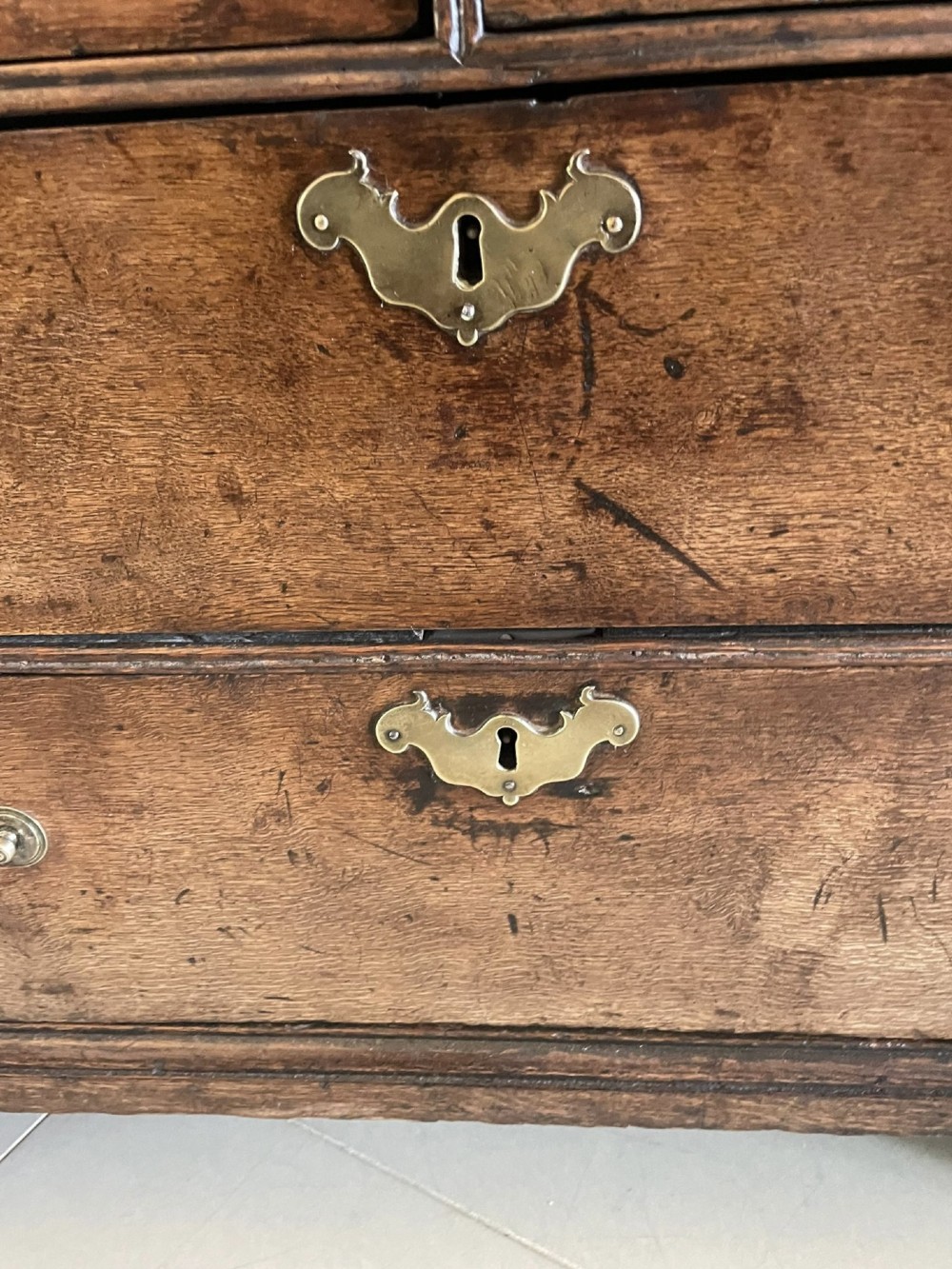 A 17th-century oak writing bureau featuring a slant-front lid above multiple drawers with brass teardrop handles and bracket feet. View VI