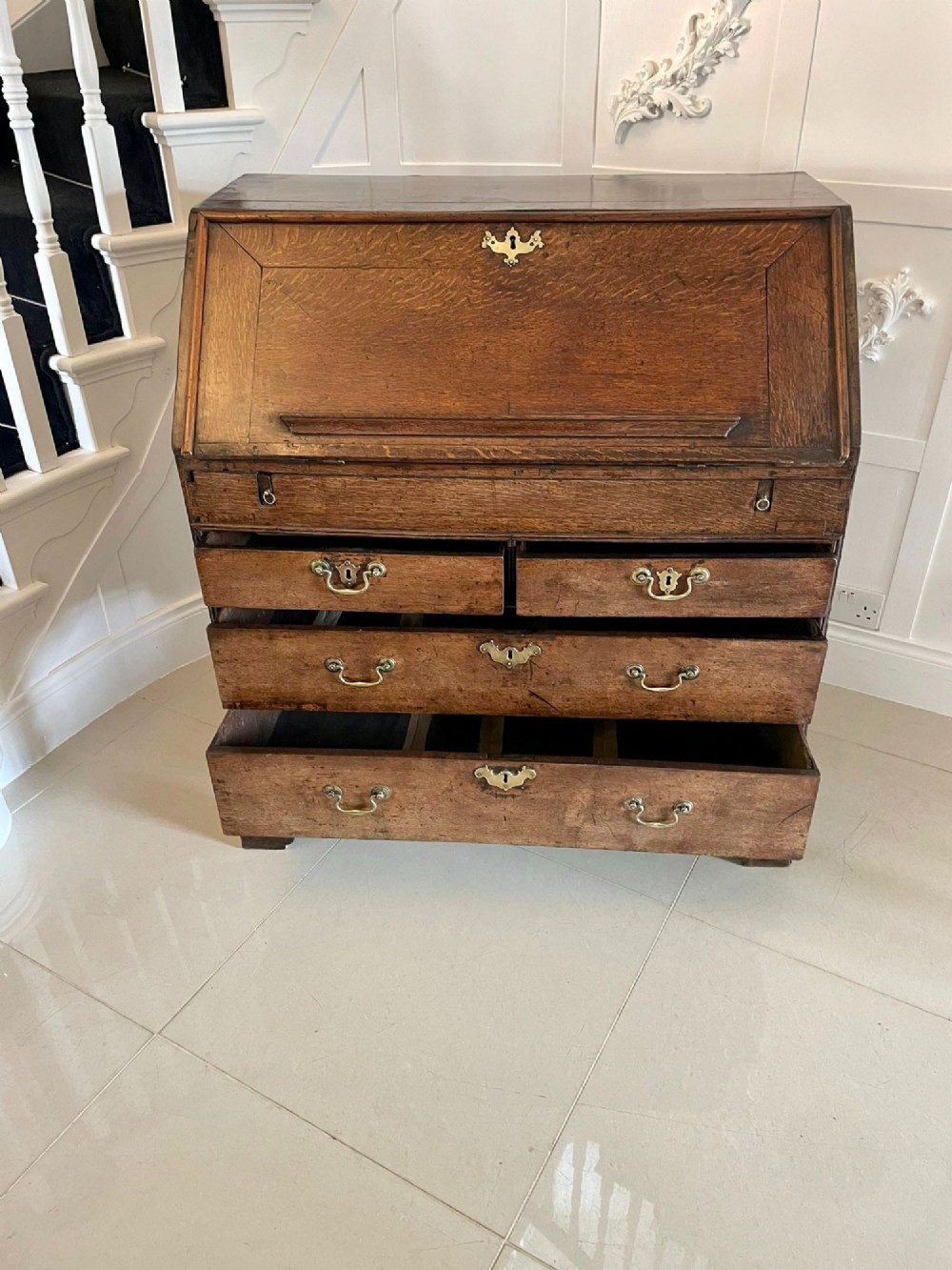 A 17th-century oak writing bureau featuring a slant-front lid above multiple drawers with brass teardrop handles and bracket feet. View VII