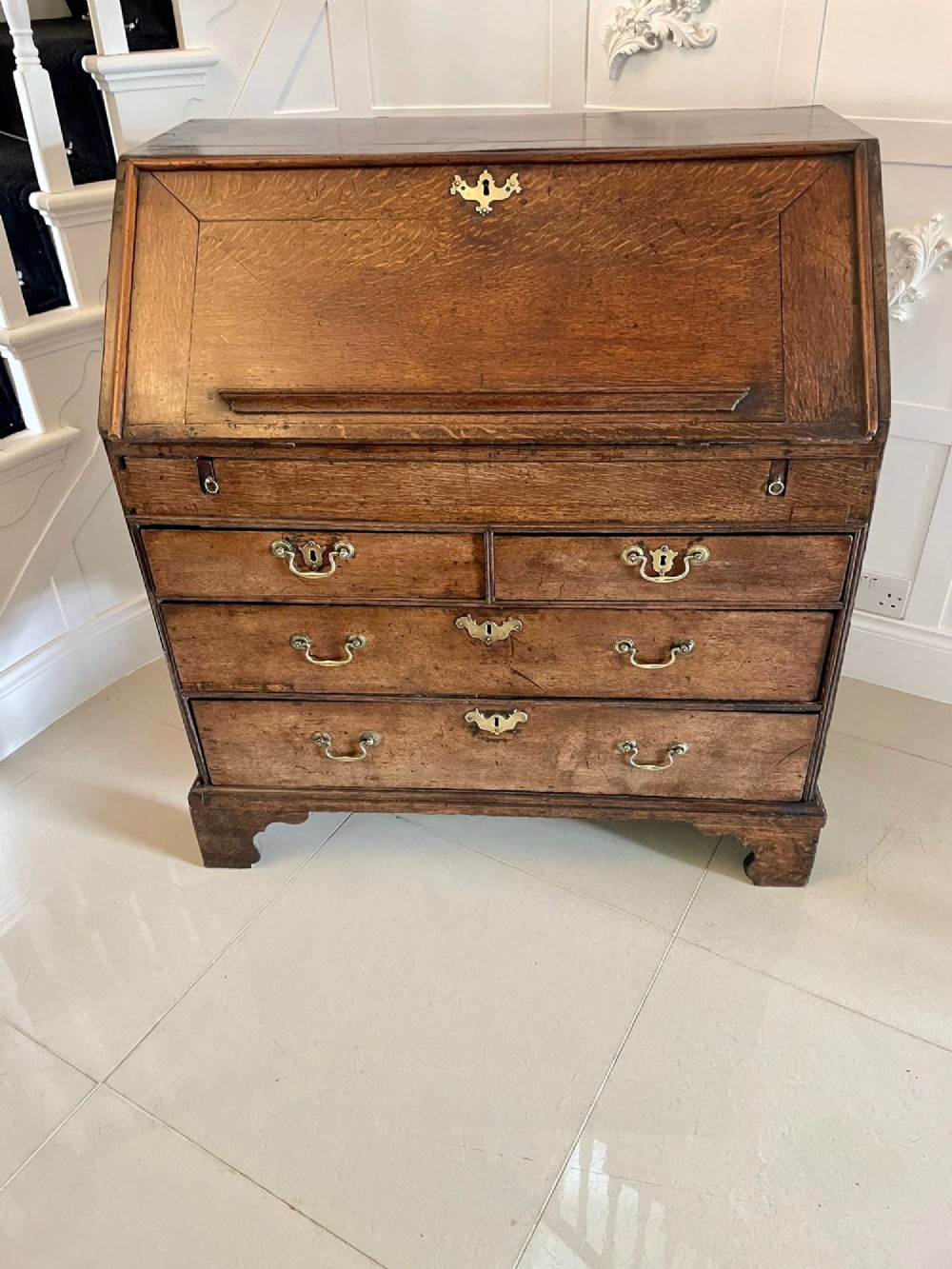 A 17th-century oak writing bureau featuring a slant-front lid above multiple drawers with brass teardrop handles and bracket feet. View IX