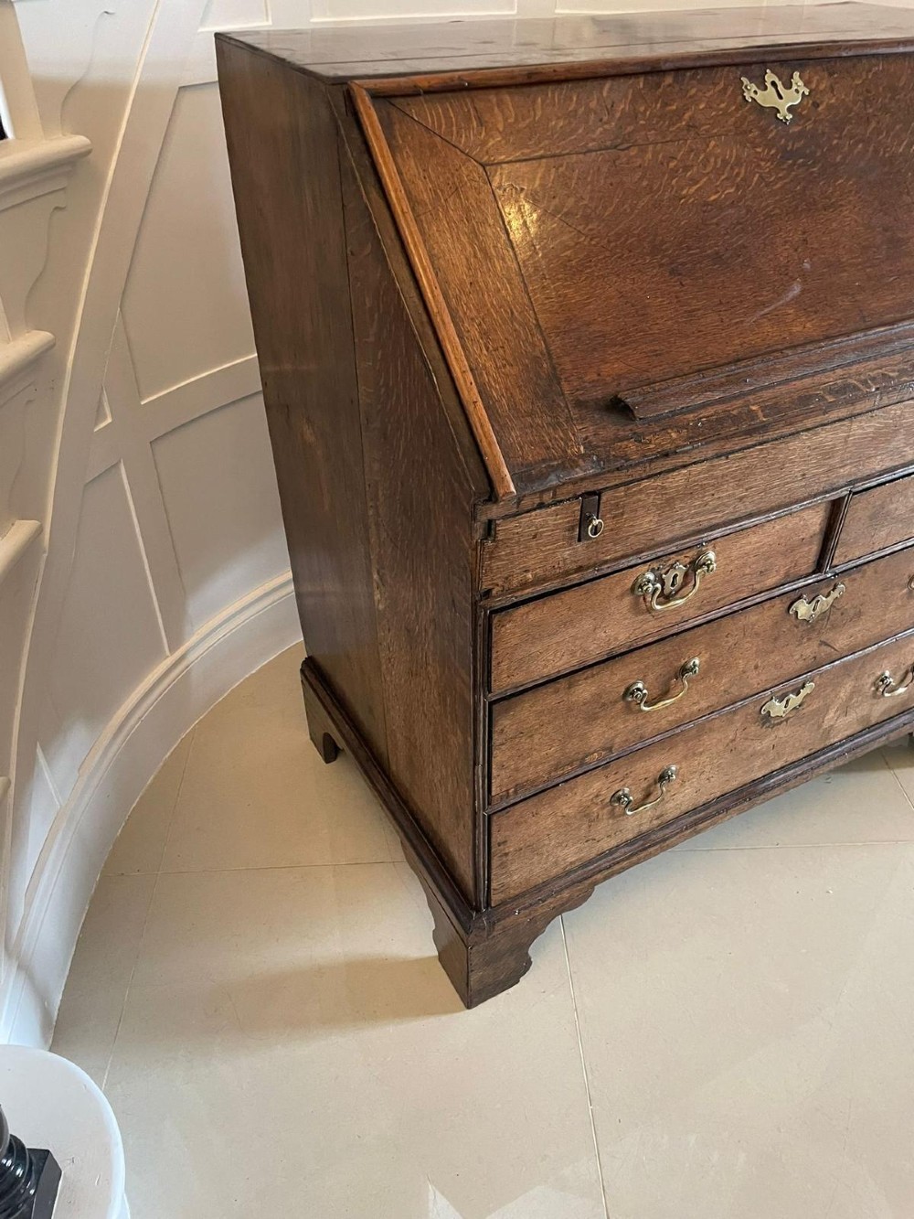 A 17th-century oak writing bureau featuring a slant-front lid above multiple drawers with brass teardrop handles and bracket feet. View X