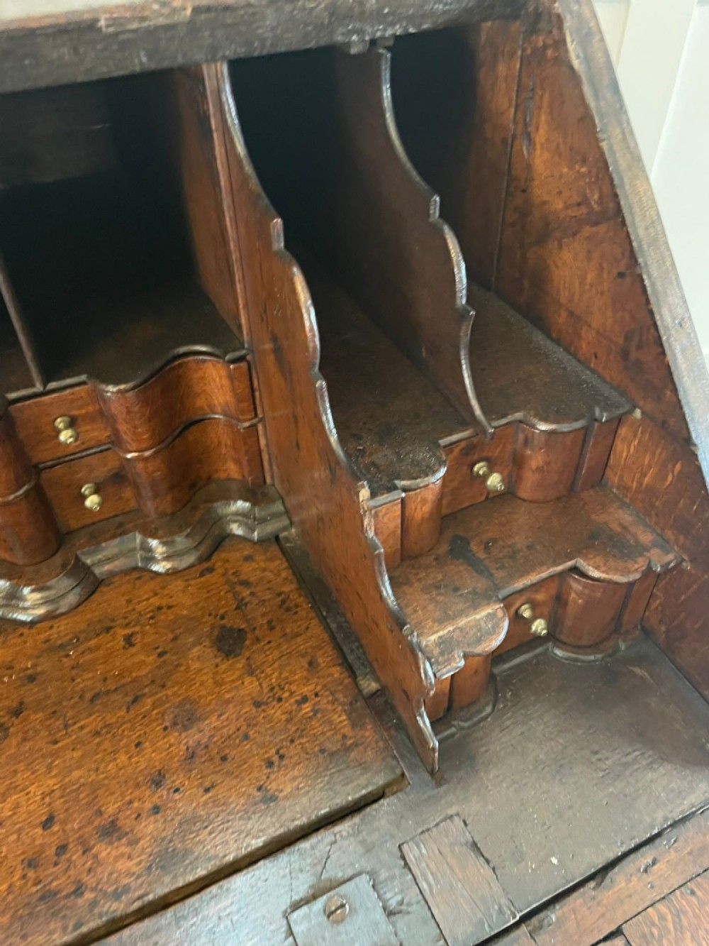 A 17th-century oak writing bureau featuring a slant-front lid above multiple drawers with brass teardrop handles and bracket feet. View XII