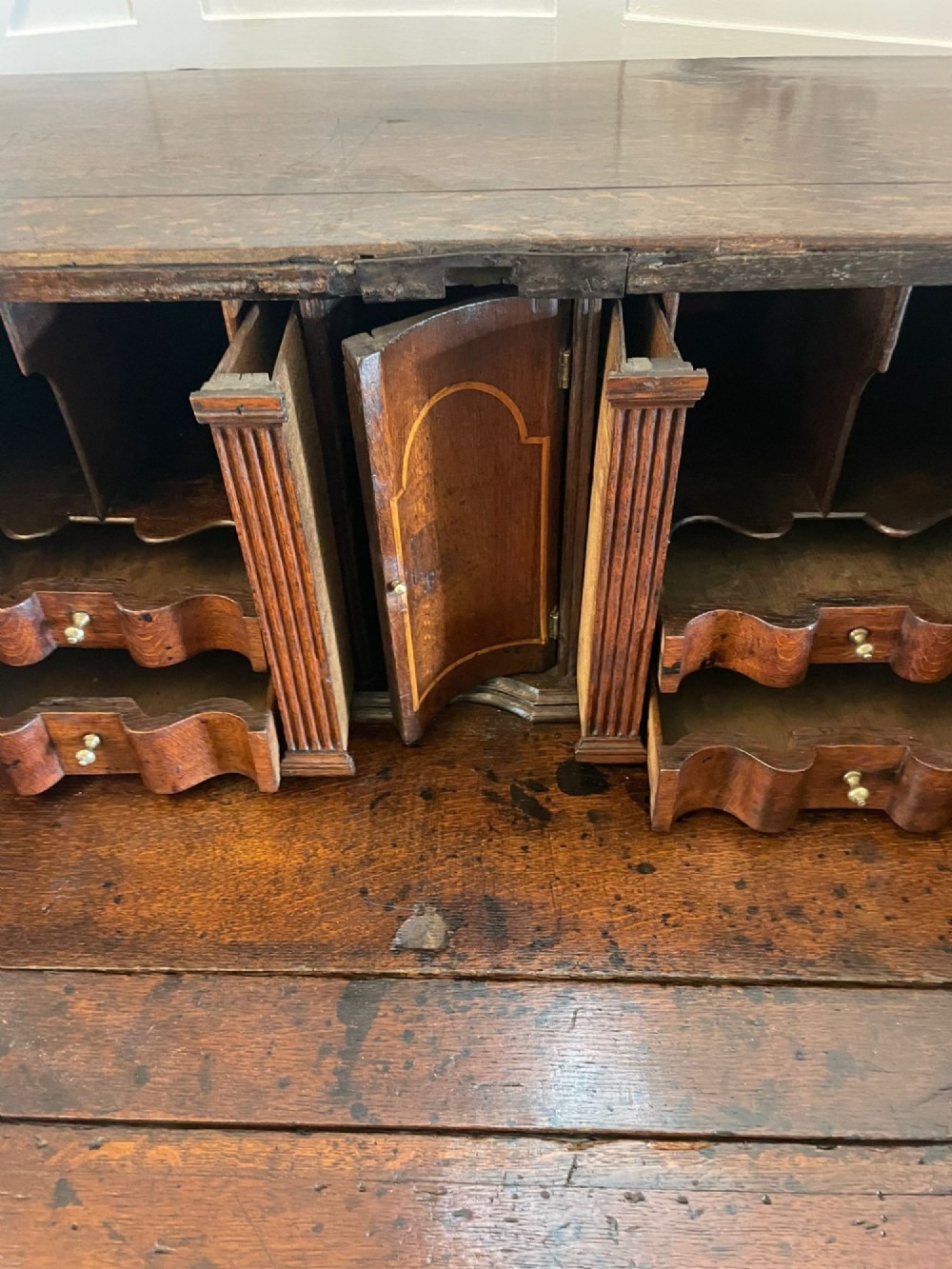 A 17th-century oak writing bureau featuring a slant-front lid above multiple drawers with brass teardrop handles and bracket feet. View XIII