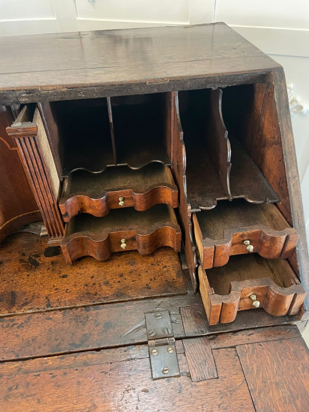 A 17th-century oak writing bureau featuring a slant-front lid above multiple drawers with brass teardrop handles and bracket feet. View XV