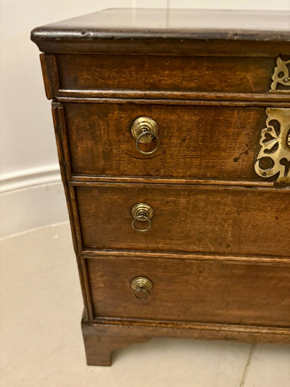 An early 18th-century dark oak box coffer styled as a miniature chest of drawers with decorative brass escutcheons, ring handles, and bracket feet. View V