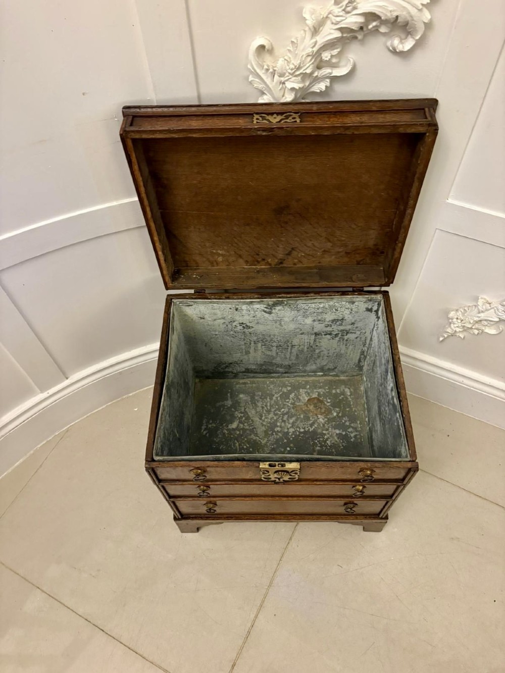 An early 18th-century dark oak box coffer styled as a miniature chest of drawers with decorative brass escutcheons, ring handles, and bracket feet. View VI
