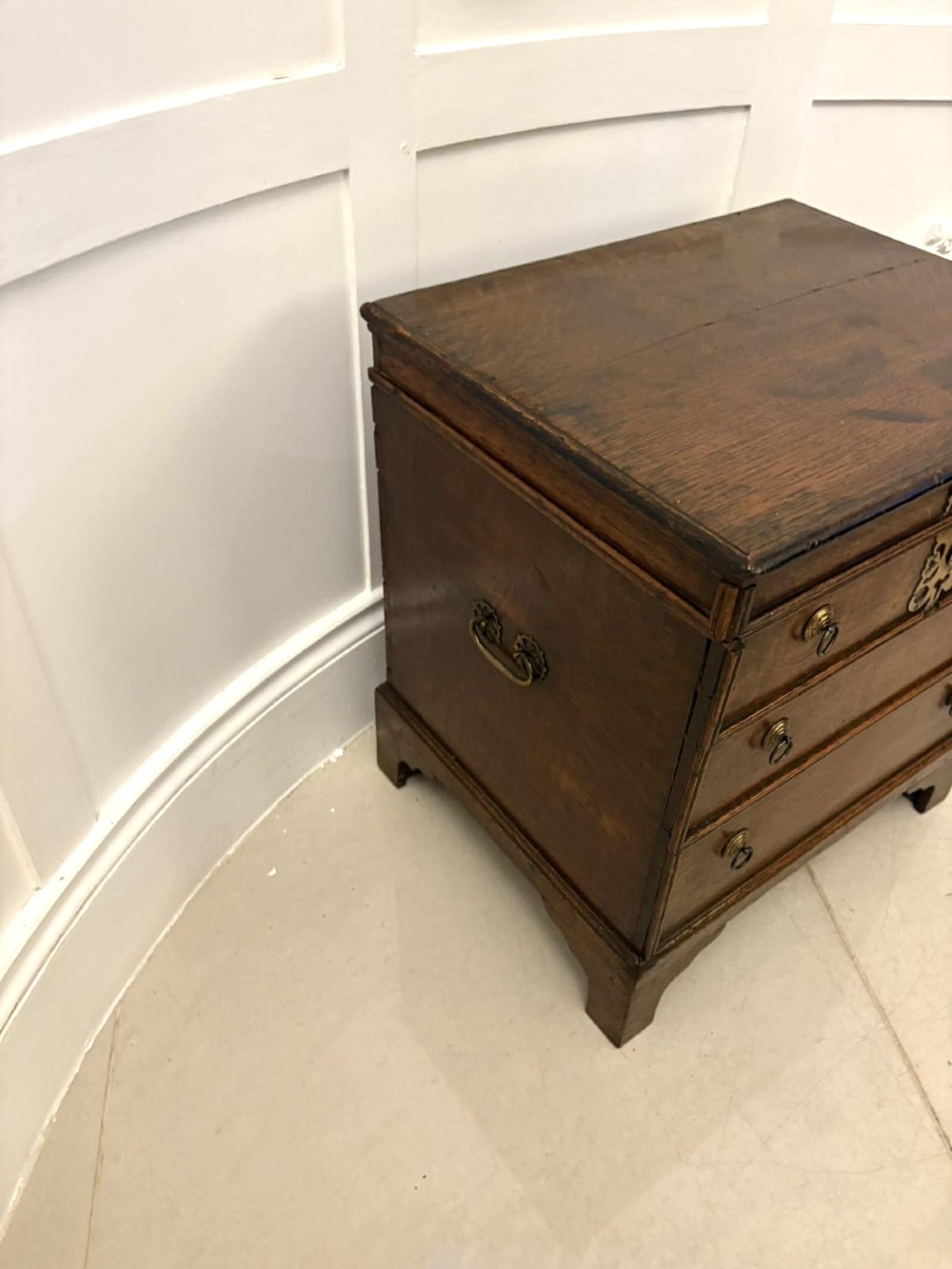 An early 18th-century dark oak box coffer styled as a miniature chest of drawers with decorative brass escutcheons, ring handles, and bracket feet. View VII