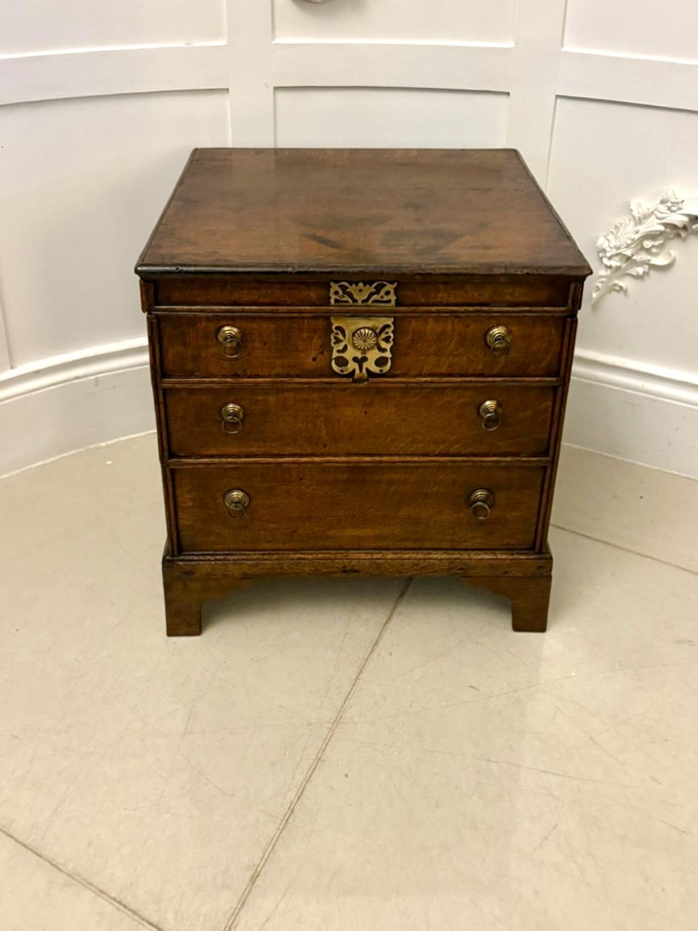 An early 18th-century dark oak box coffer styled as a miniature chest of drawers with decorative brass escutcheons, ring handles, and bracket feet. View XI
