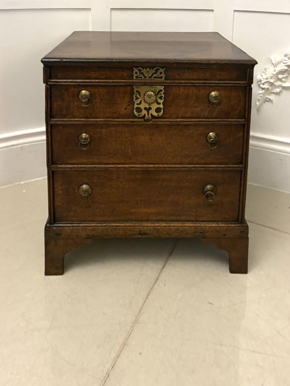 An early 18th-century dark oak box coffer styled as a miniature chest of drawers with decorative brass escutcheons, ring handles, and bracket feet.