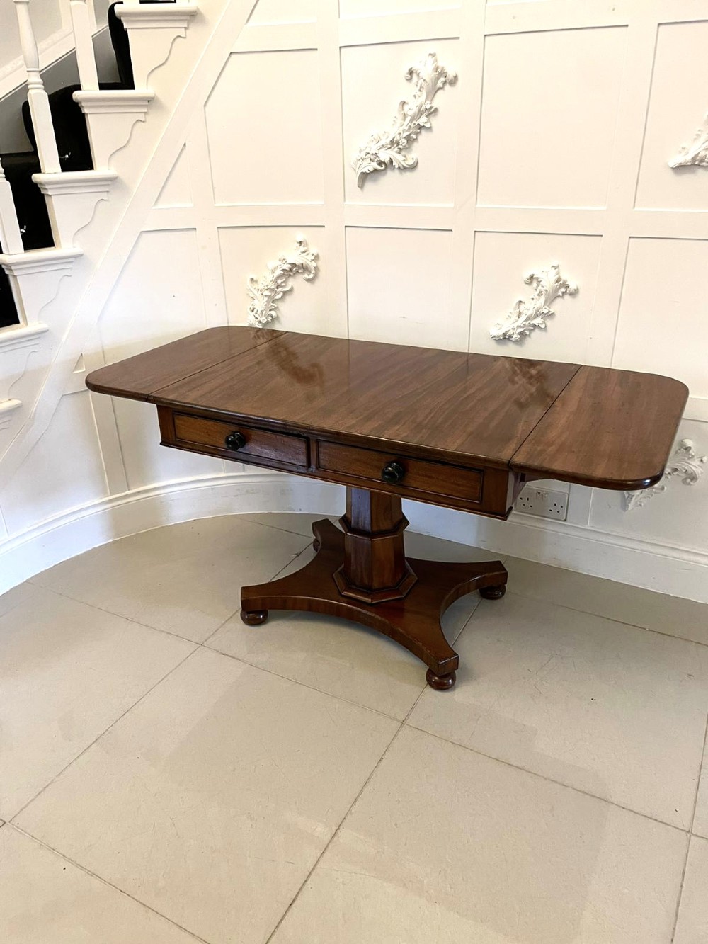 A Regency mahogany sofa table featuring two short drawers with black turned knobs, twin drop-leaf flaps, a central octagonal pedestal, and a quadruped base. View VI