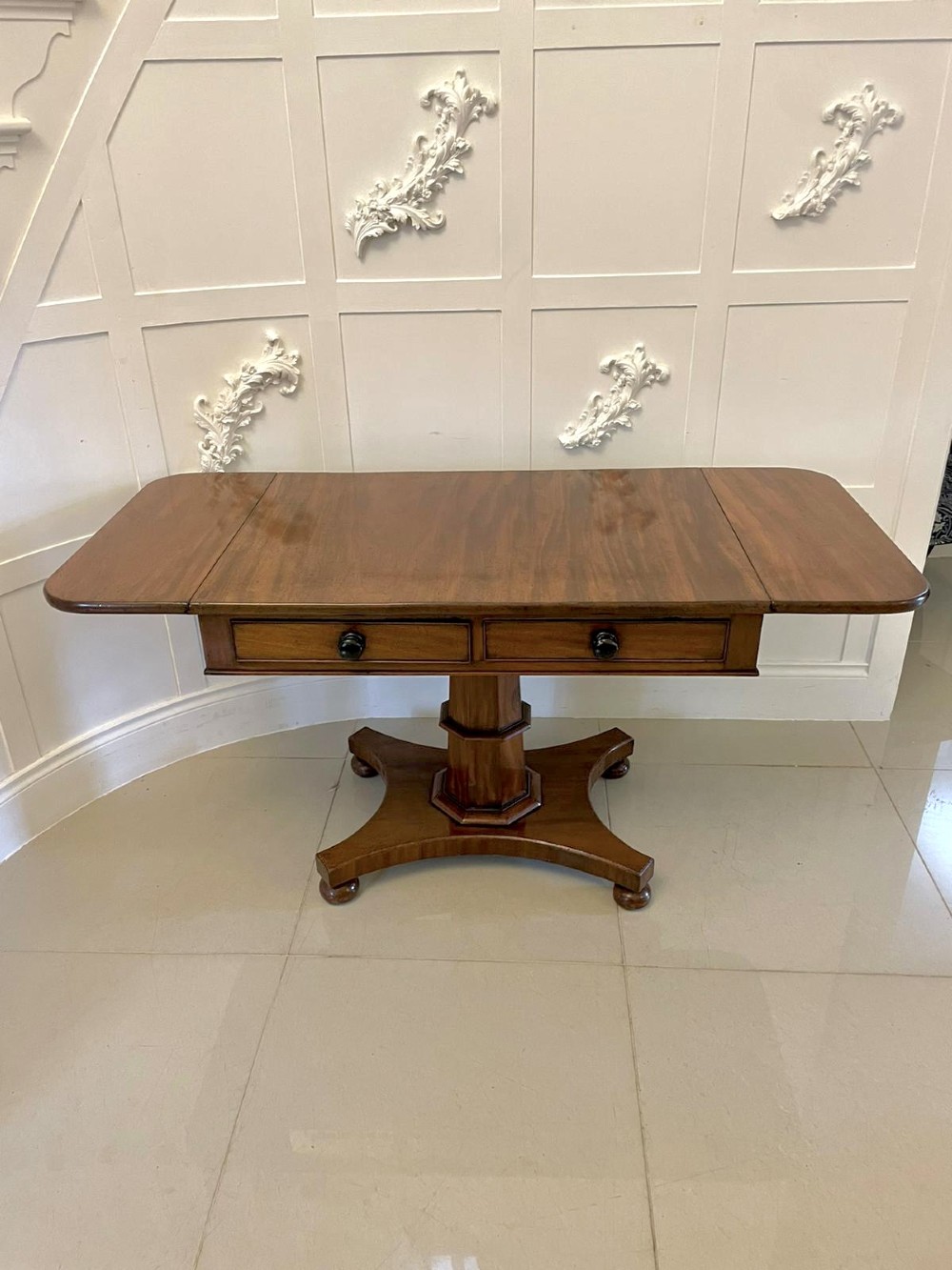 A Regency mahogany sofa table featuring two short drawers with black turned knobs, twin drop-leaf flaps, a central octagonal pedestal, and a quadruped base. View VII