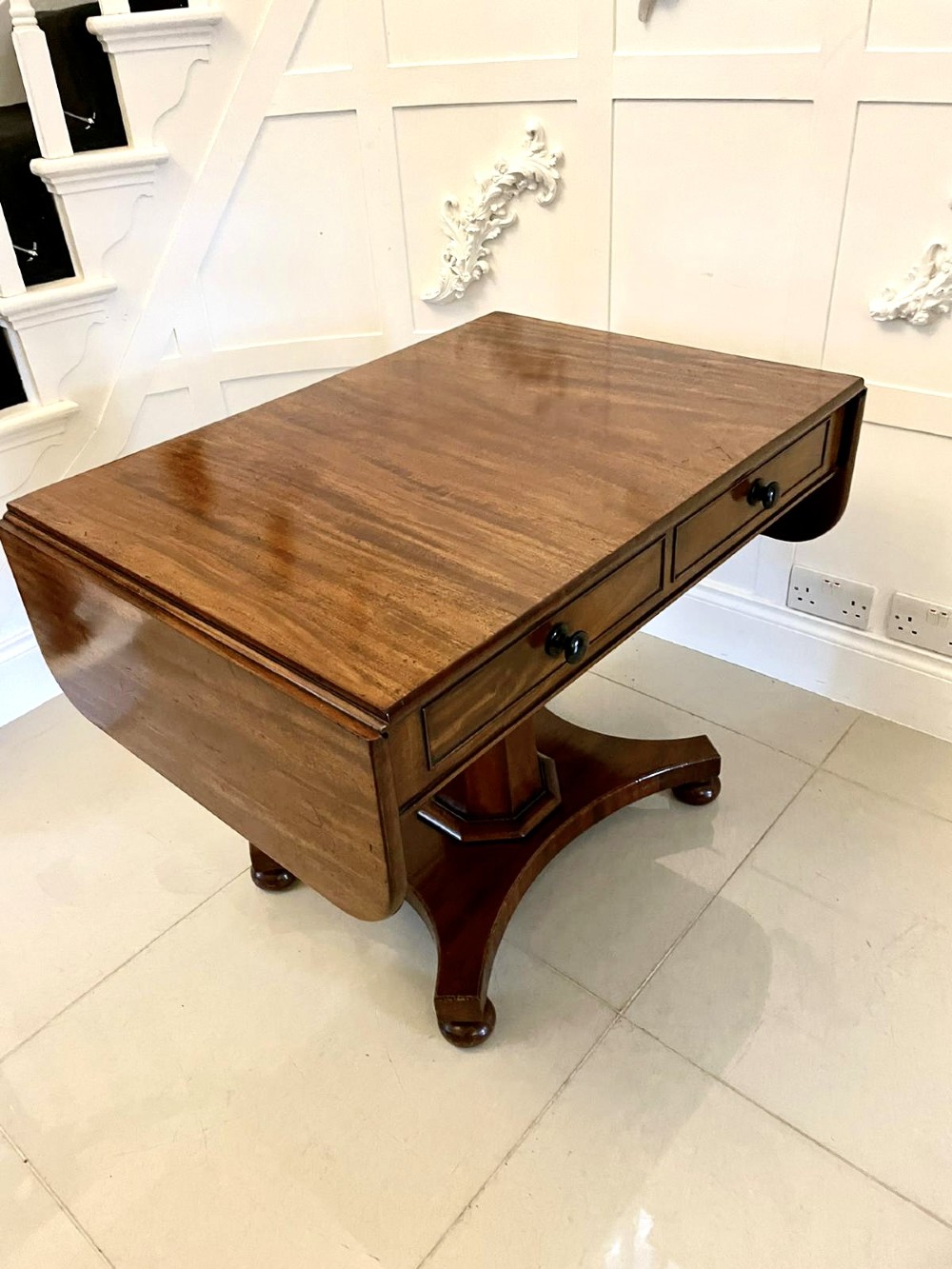 A Regency mahogany sofa table featuring two short drawers with black turned knobs, twin drop-leaf flaps, a central octagonal pedestal, and a quadruped base. View X