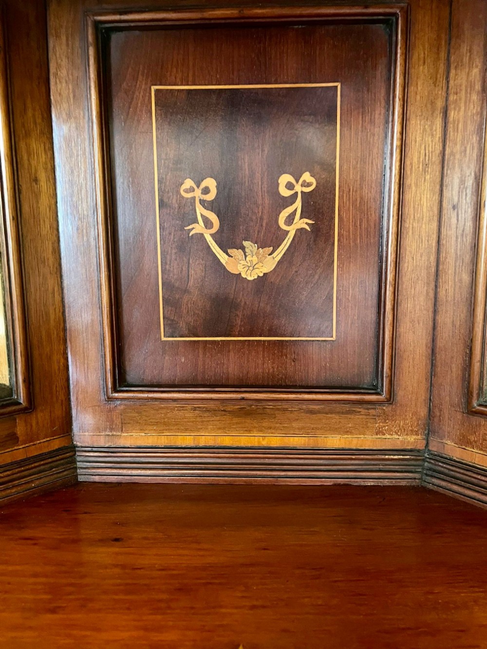 An Edwardian mahogany corner display cabinet featuring floral satinwood inlay, glazed doors with astragal bars, and a mirrored central niche. View IX