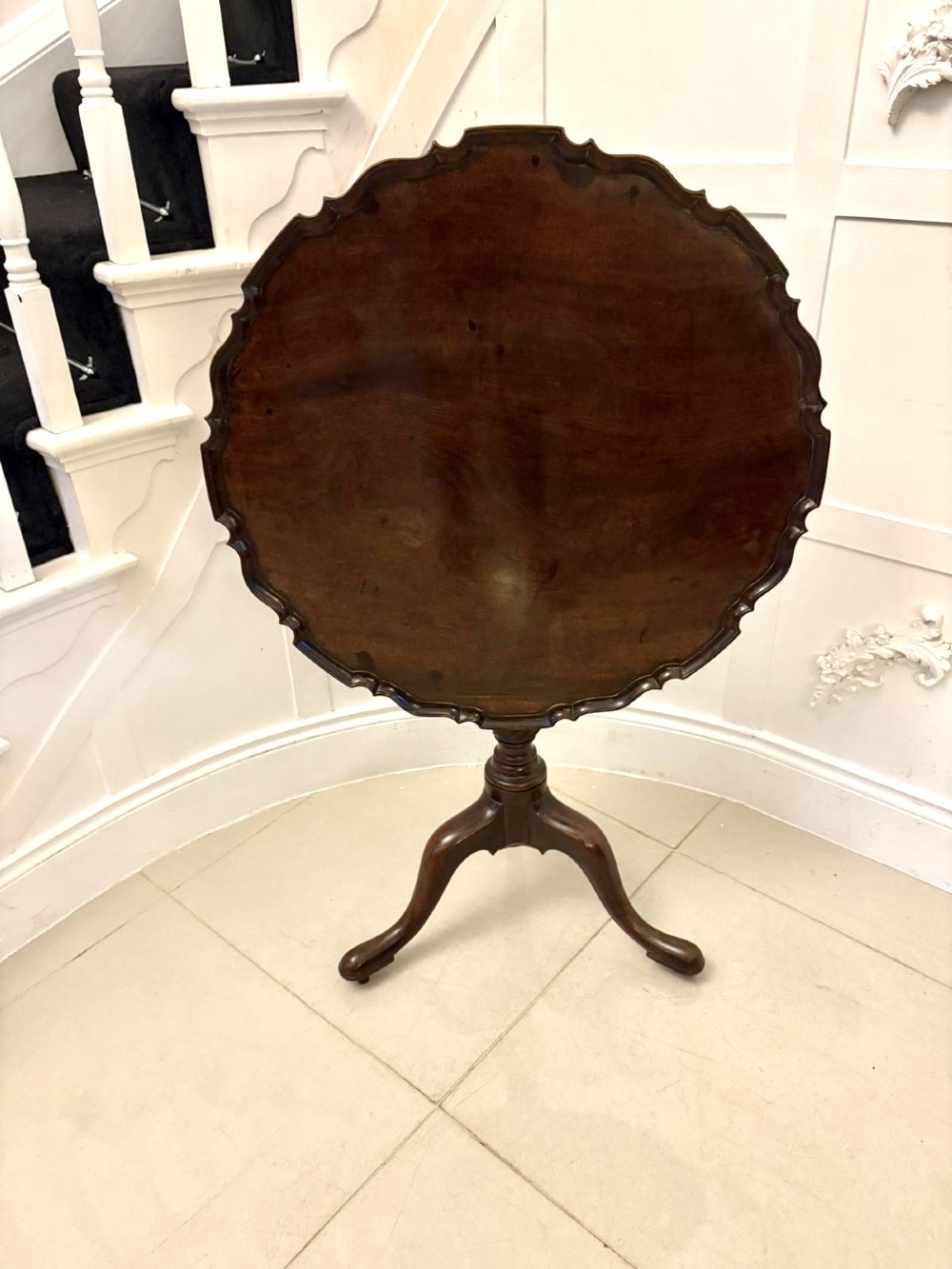 An 18th-century mahogany Chippendale tilt-top tripod table shown upright with a scalloped piecrust edge, turned column, and three cabriole legs.