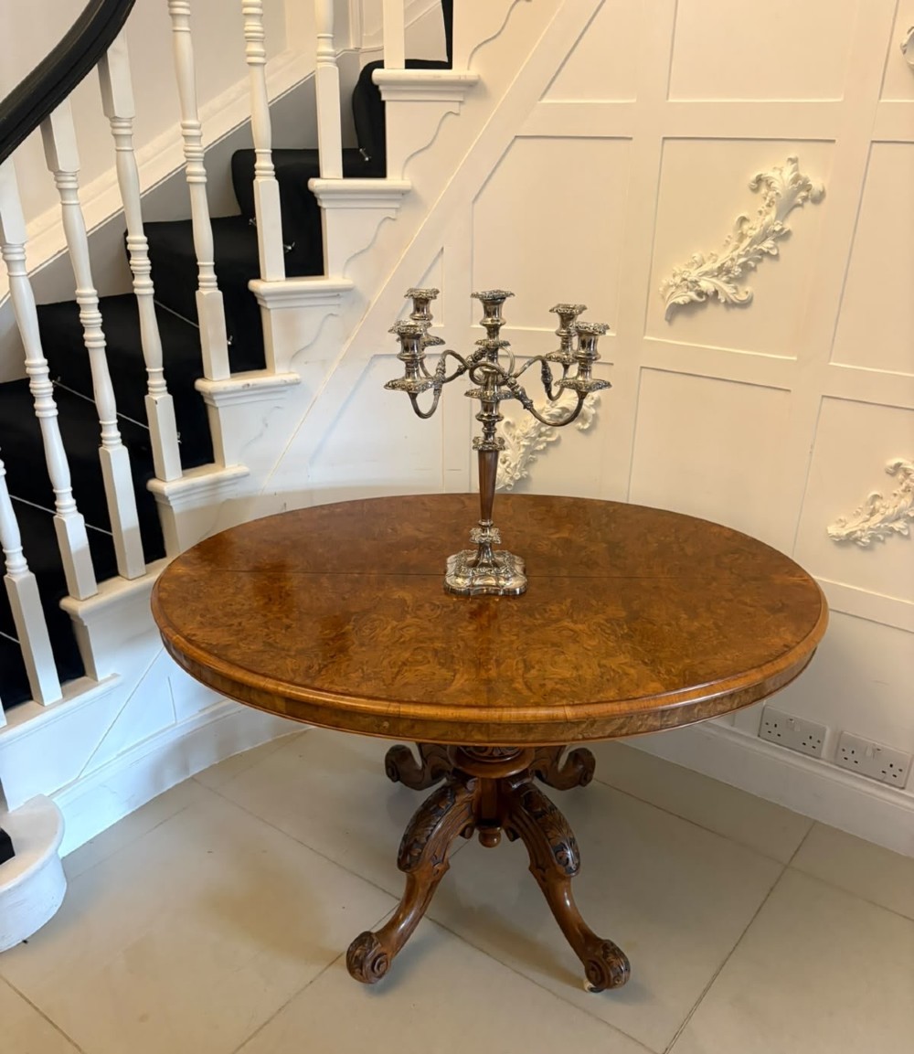 An antique Victorian oval tilt-top table made of burr walnut with a four-star carved pedestal base and white ceramic castors, shown with the tabletop tilted vertically. View IV