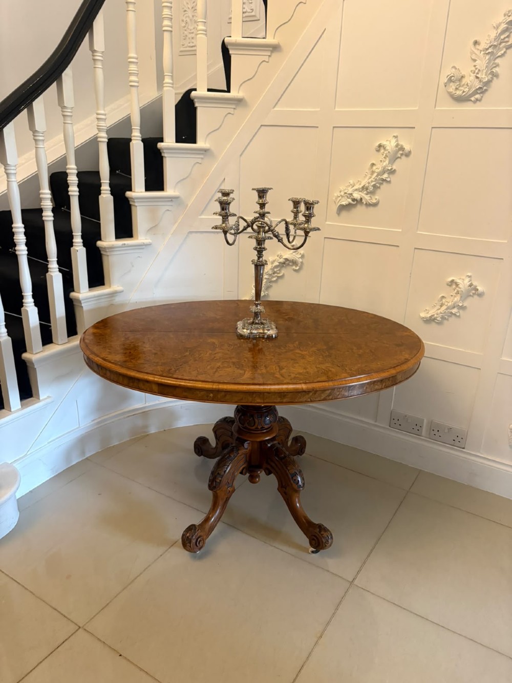 An antique Victorian oval tilt-top table made of burr walnut with a four-star carved pedestal base and white ceramic castors, shown with the tabletop tilted vertically. View X