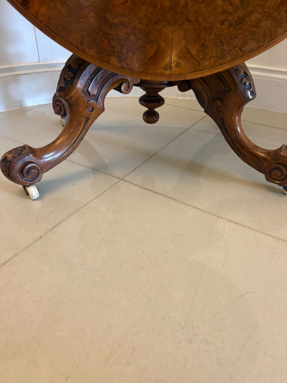 An antique Victorian oval tilt-top table made of burr walnut with a four-star carved pedestal base and white ceramic castors, shown with the tabletop tilted vertically. View XV