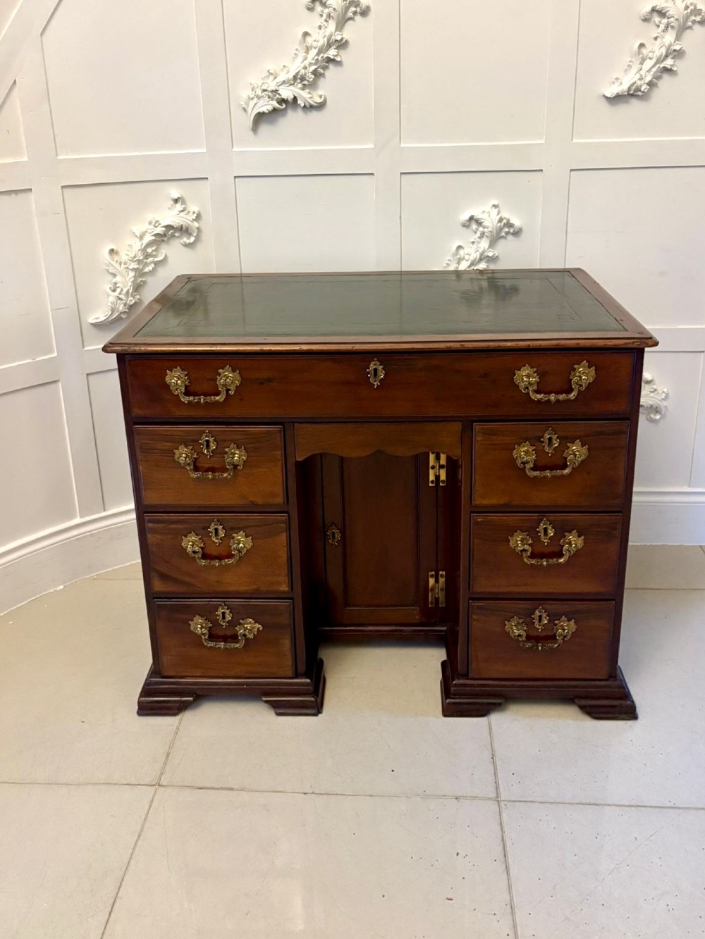 A George III mahogany kneehole desk with a green leather inset top, brass handles, six side drawers, and a central recessed cupboard on bracket feet.