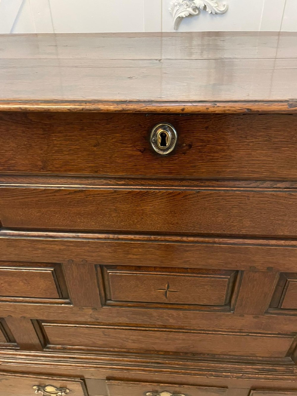 An 18th-century oak coffer elevated on a stand, with geometric panel moulding across the front lid section, lower brass-handled drawers, and square legs. View III