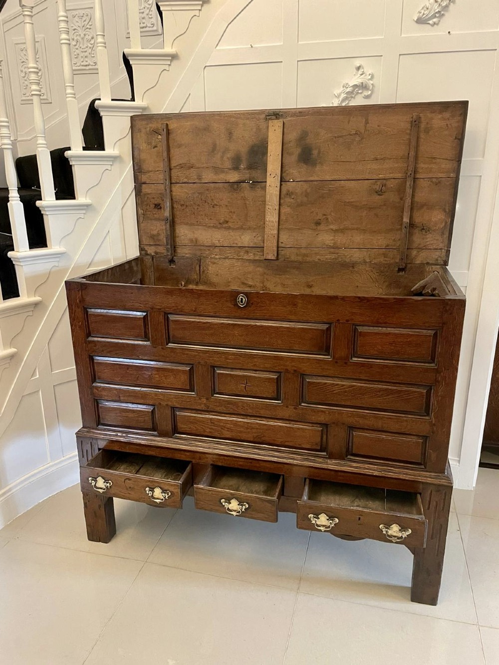 An 18th-century oak coffer elevated on a stand, with geometric panel moulding across the front lid section, lower brass-handled drawers, and square legs. View VII