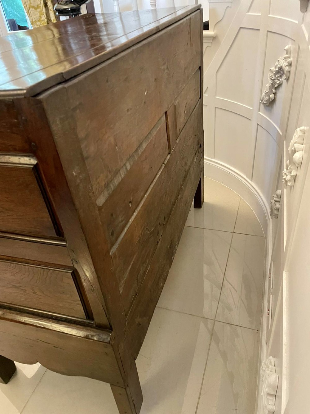An 18th-century oak coffer elevated on a stand, with geometric panel moulding across the front lid section, lower brass-handled drawers, and square legs. View IX