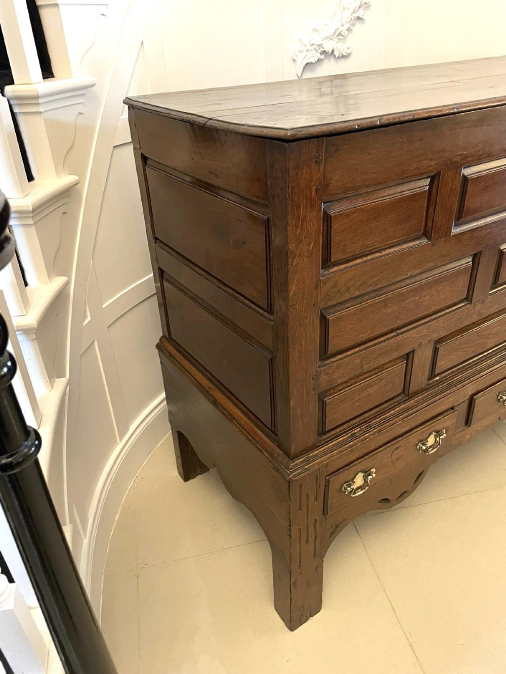 An 18th-century oak coffer elevated on a stand, with geometric panel moulding across the front lid section, lower brass-handled drawers, and square legs. View XIV