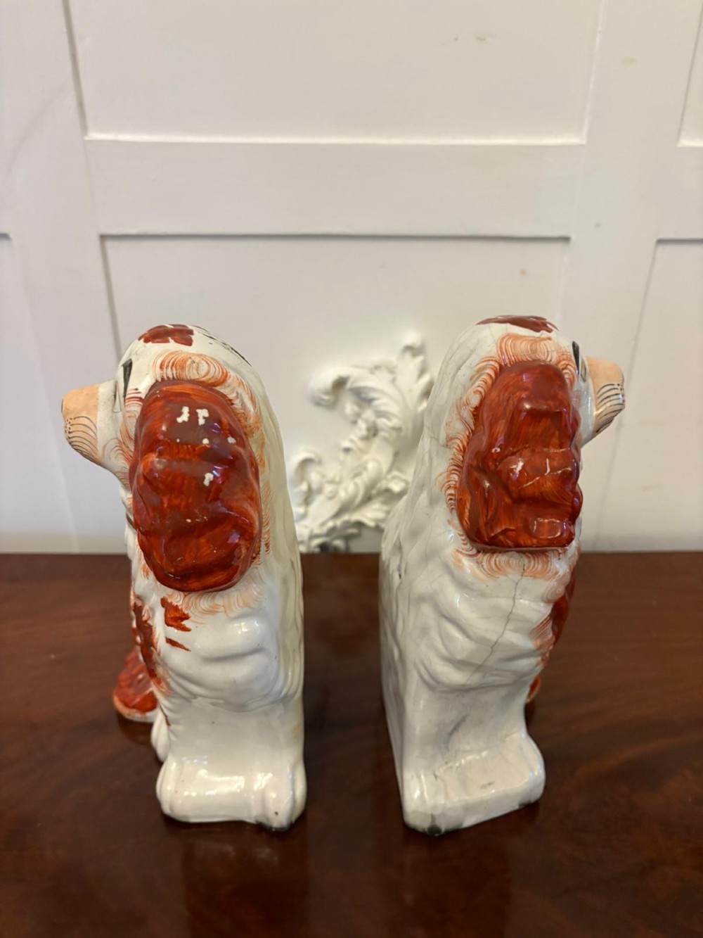 A pair of Victorian Staffordshire ceramic spaniel figurines with painted russet spots and black chain collars seated on a dark wooden surface. View II