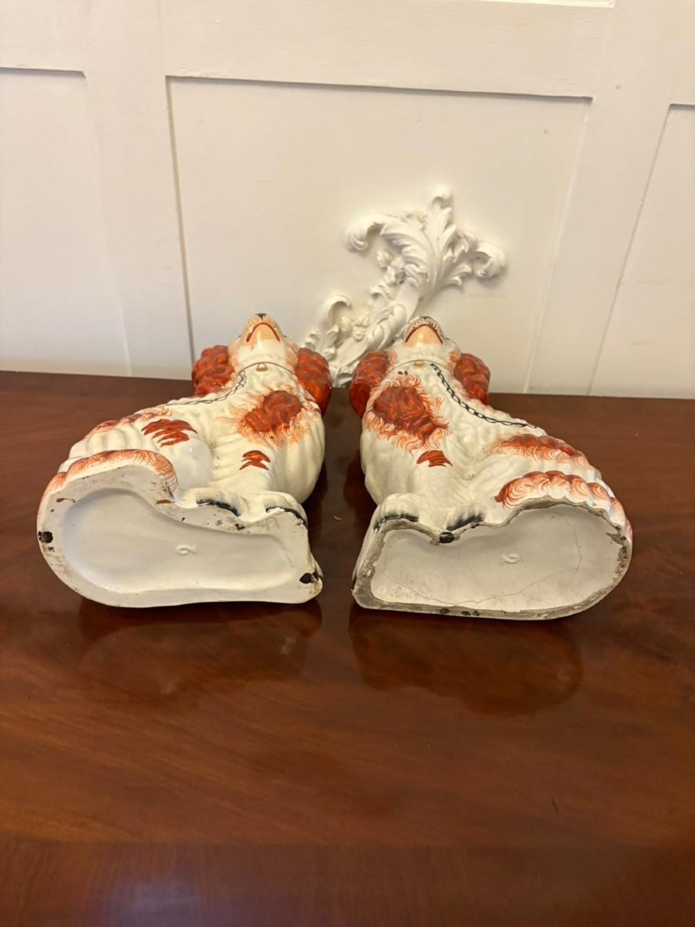 A pair of Victorian Staffordshire ceramic spaniel figurines with painted russet spots and black chain collars seated on a dark wooden surface. View III