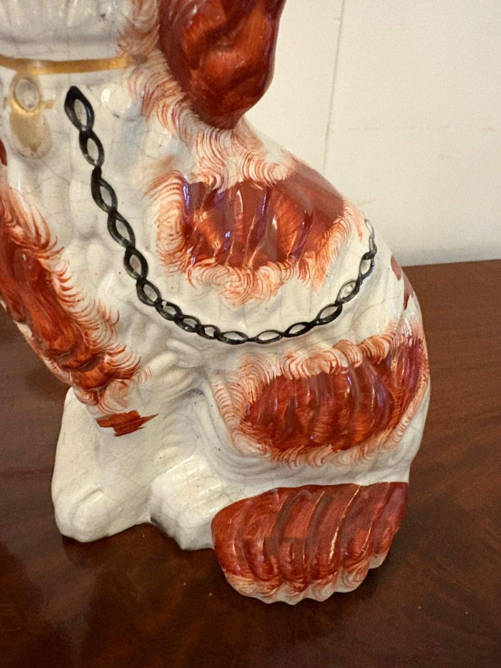 A pair of Victorian Staffordshire ceramic spaniel figurines with painted russet spots and black chain collars seated on a dark wooden surface. View IV