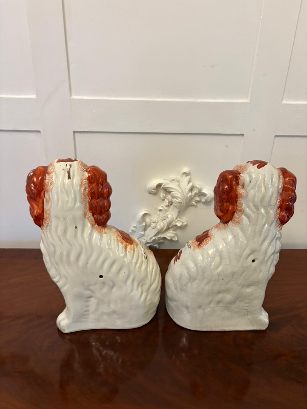 A pair of Victorian Staffordshire ceramic spaniel figurines with painted russet spots and black chain collars seated on a dark wooden surface. View V
