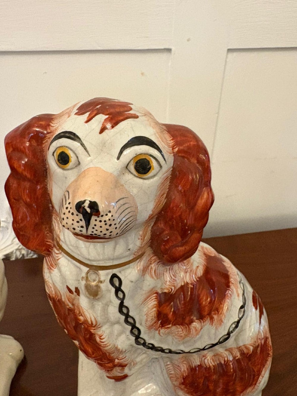 A pair of Victorian Staffordshire ceramic spaniel figurines with painted russet spots and black chain collars seated on a dark wooden surface. View VI