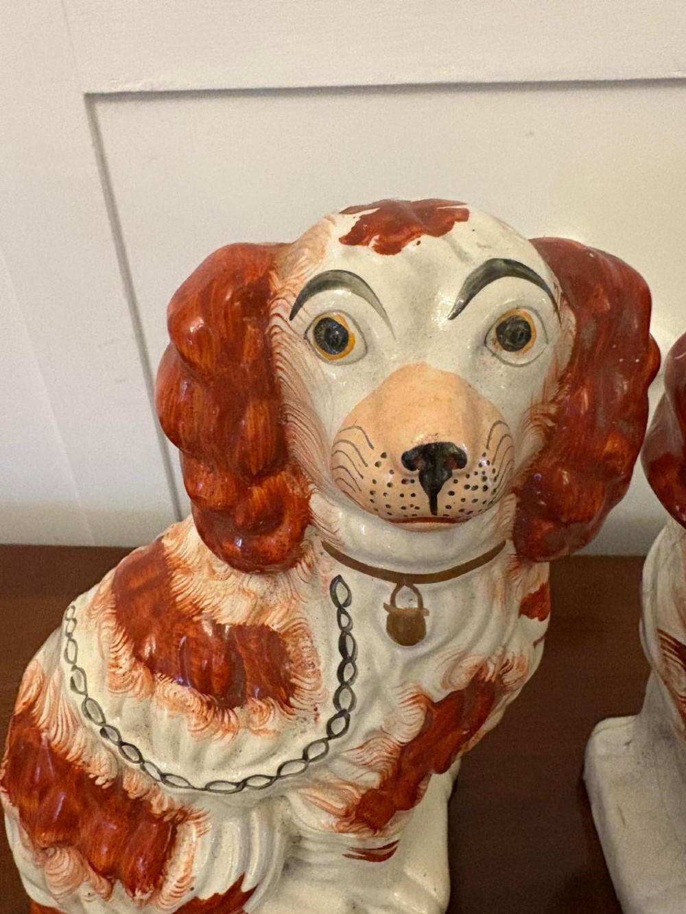 A pair of Victorian Staffordshire ceramic spaniel figurines with painted russet spots and black chain collars seated on a dark wooden surface. View VII