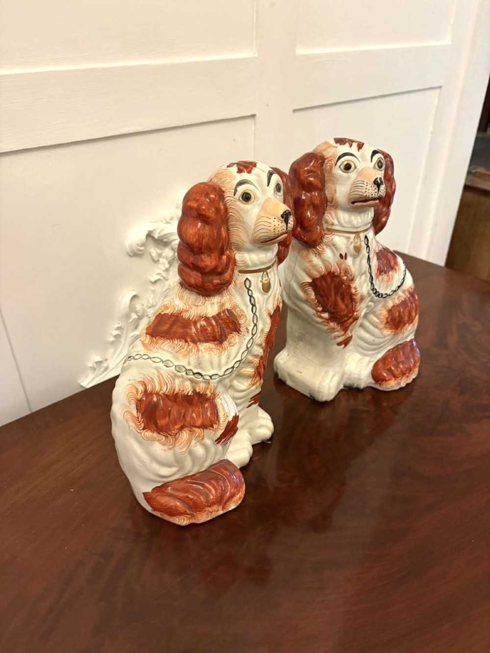 A pair of Victorian Staffordshire ceramic spaniel figurines with painted russet spots and black chain collars seated on a dark wooden surface. View VIII