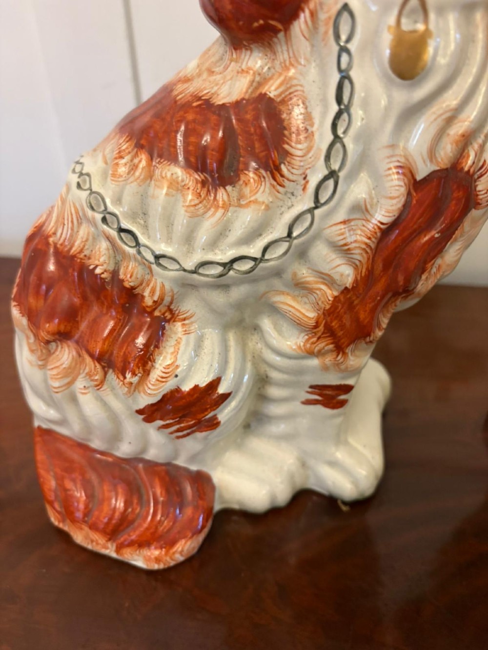 A pair of Victorian Staffordshire ceramic spaniel figurines with painted russet spots and black chain collars seated on a dark wooden surface. View IX