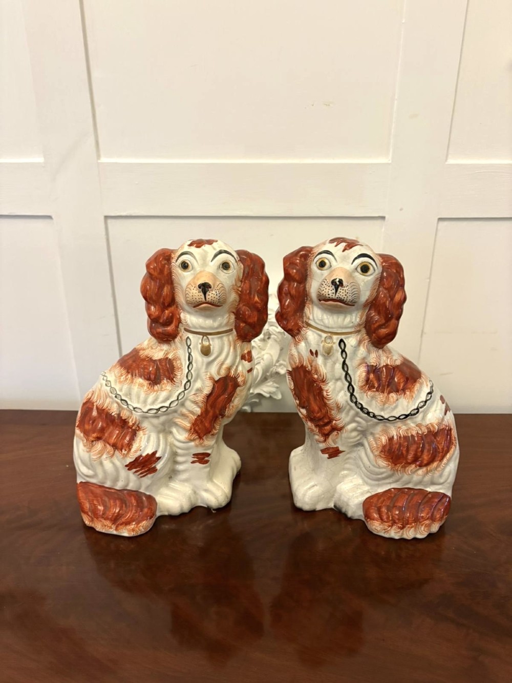 A pair of Victorian Staffordshire ceramic spaniel figurines with painted russet spots and black chain collars seated on a dark wooden surface.