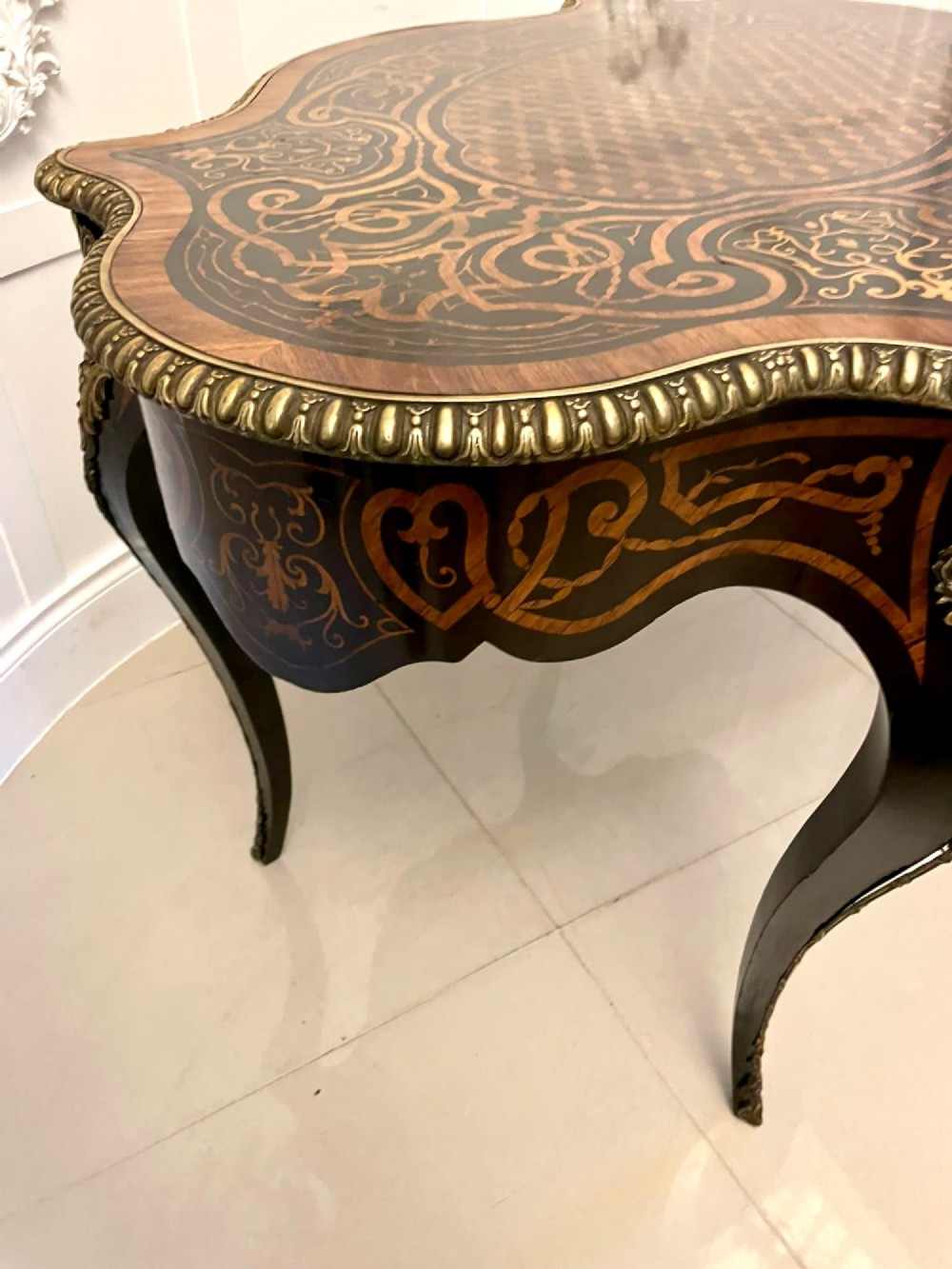 An antique French Rococo Revival centre table featuring detailed marquetry and parquetry wood patterns, serpentine edges, brass ormolu mounts, and curved cabriole legs. View VII