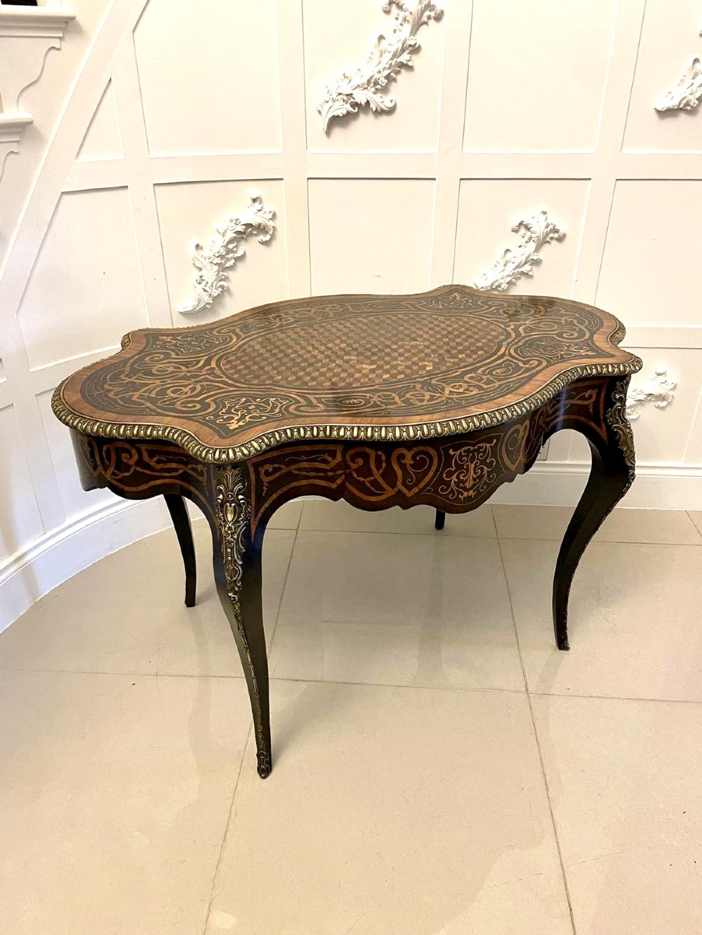An antique French Rococo Revival centre table featuring detailed marquetry and parquetry wood patterns, serpentine edges, brass ormolu mounts, and curved cabriole legs.