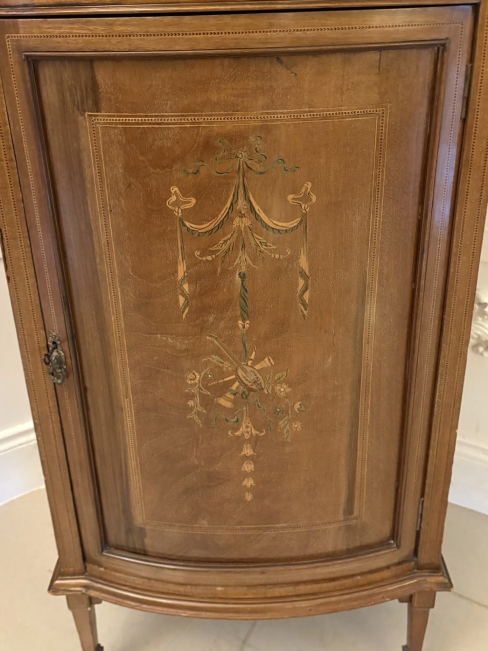 An Edwardian mahogany bow-fronted side cabinet featuring ribbon and urn marquetry inlay, a raised gallery back, and tapered square legs. View VII