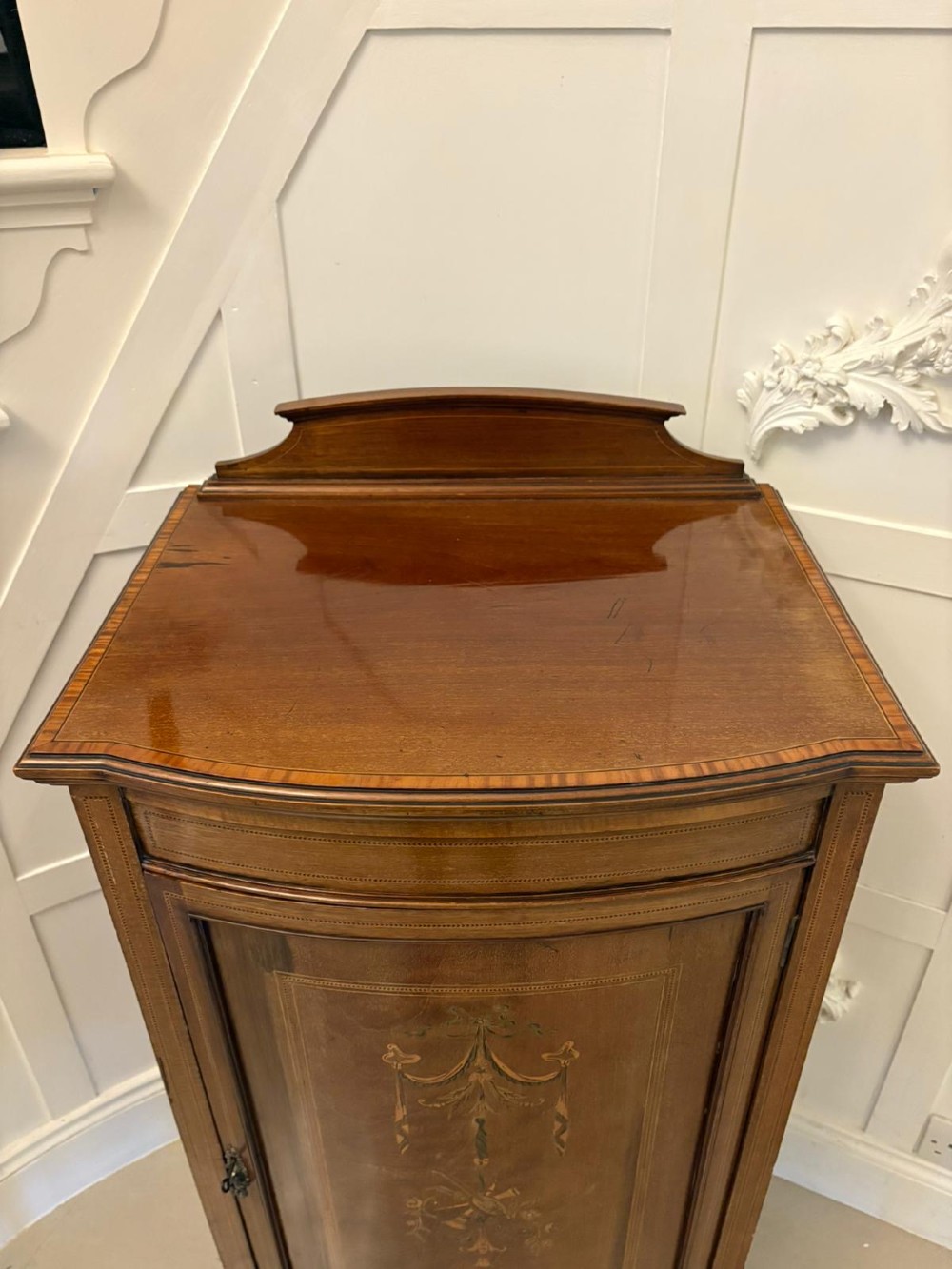 An Edwardian mahogany bow-fronted side cabinet featuring ribbon and urn marquetry inlay, a raised gallery back, and tapered square legs. View VIII