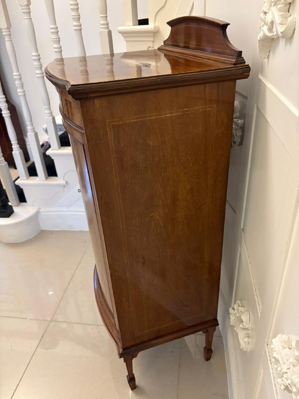 An Edwardian mahogany bow-fronted side cabinet featuring ribbon and urn marquetry inlay, a raised gallery back, and tapered square legs. View IX