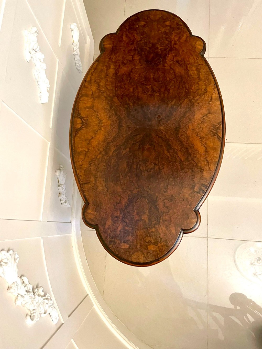 An antique Victorian oval centre table featuring a figured burr walnut top with moulded edges, carved end supports, a turned stretcher, and brass castors. View II
