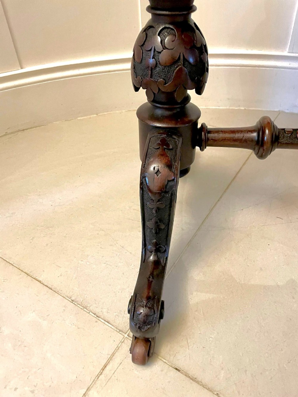 An antique Victorian oval centre table featuring a figured burr walnut top with moulded edges, carved end supports, a turned stretcher, and brass castors. View III