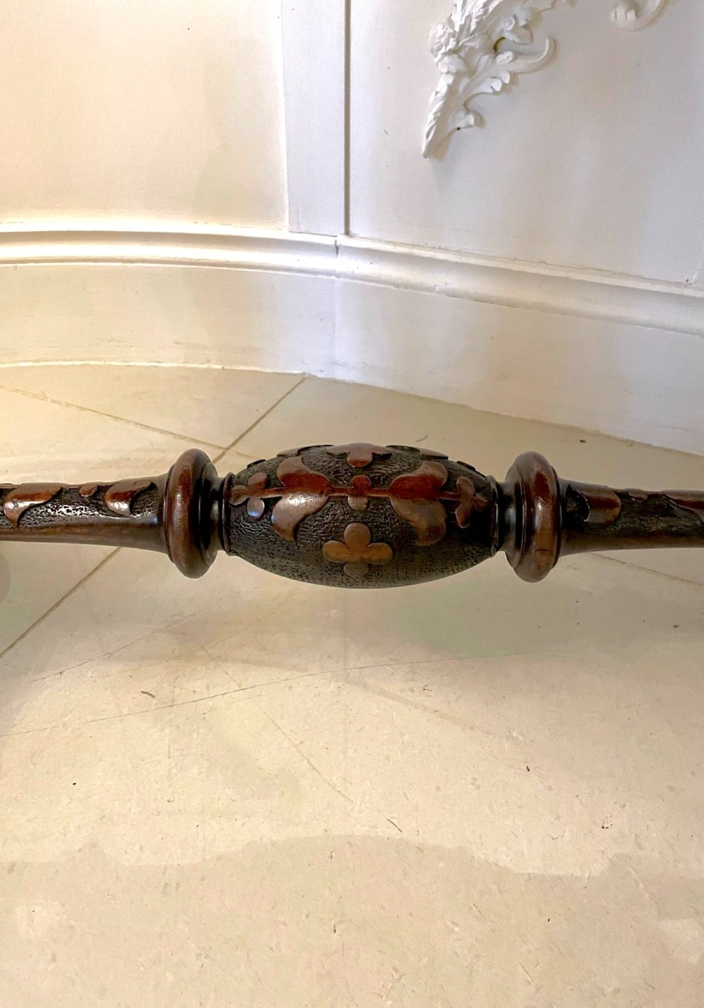 An antique Victorian oval centre table featuring a figured burr walnut top with moulded edges, carved end supports, a turned stretcher, and brass castors. View X