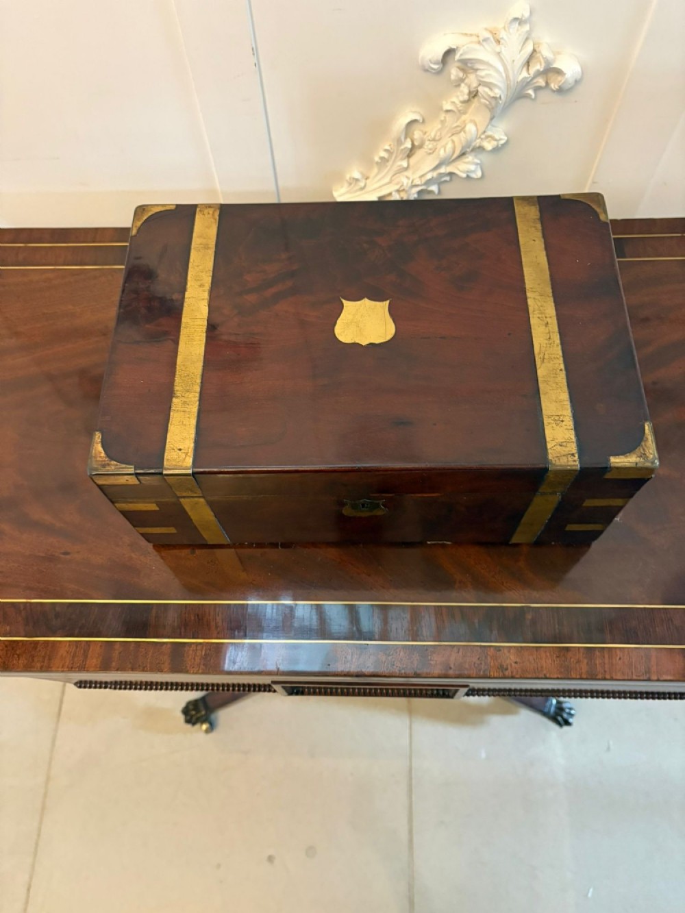 A rectangular Victorian mahogany writing box featuring brass corner brackets, vertical brass strapping, a central brass shield inlay, and a brass keyhole escutcheon. View V