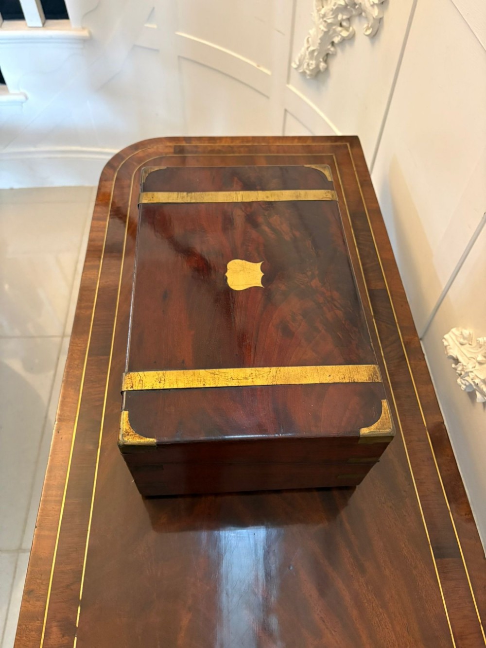 A rectangular Victorian mahogany writing box featuring brass corner brackets, vertical brass strapping, a central brass shield inlay, and a brass keyhole escutcheon. View X