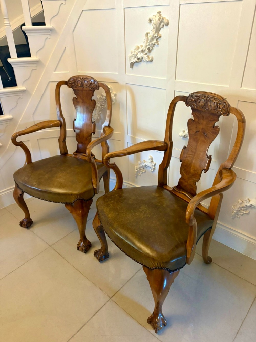 A pair of carved walnut desk armchairs featuring vasiform splats, green leather seats with brass studding, and cabriole legs ending in ball and claw feet. View X