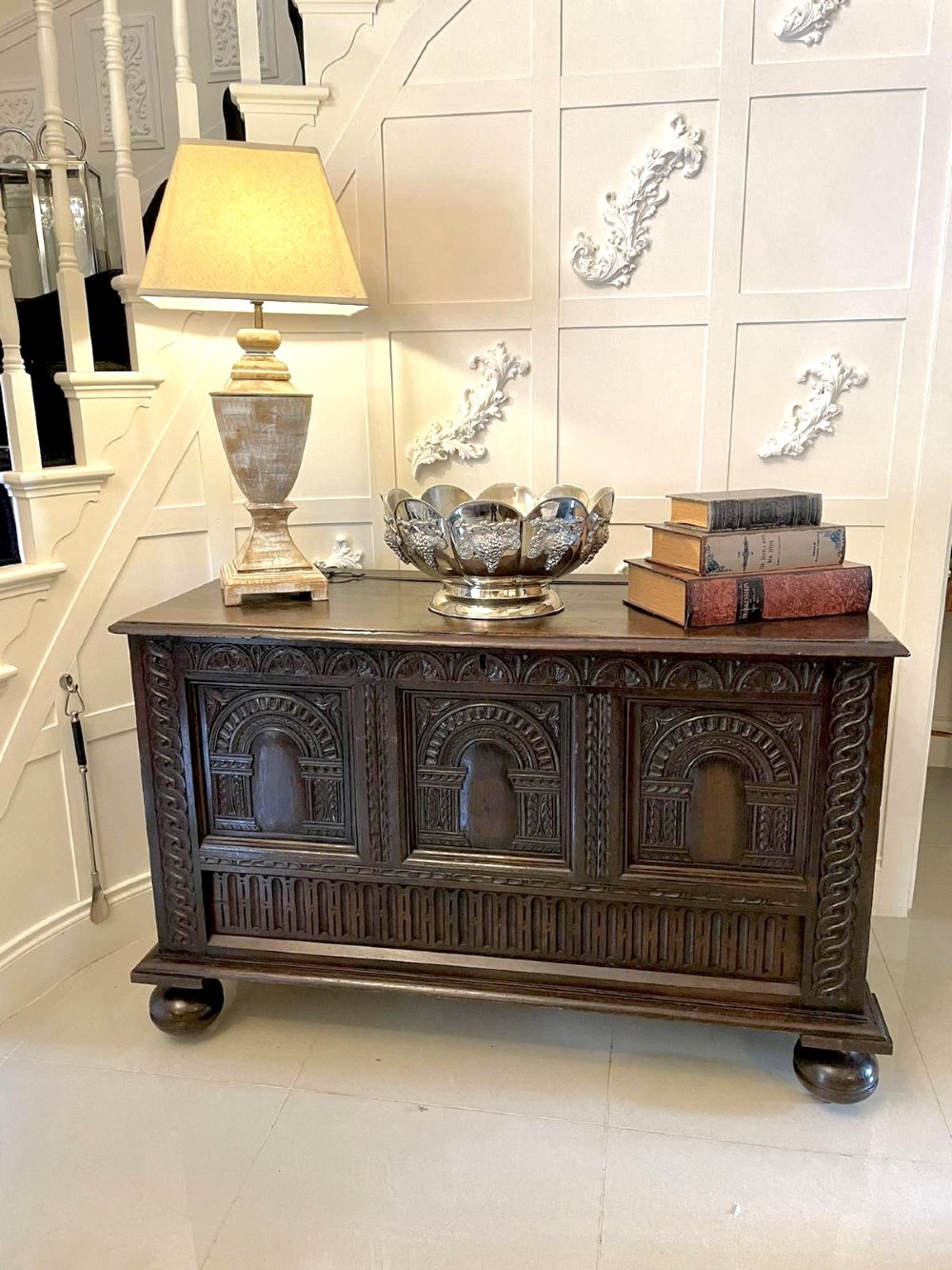 A dark carved oak coffer featuring three arcaded front panels, carved border details, top iron hinges, and turned bun feet. View II